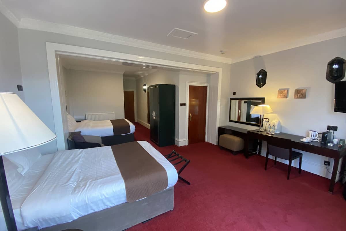 A hotel room with two beds, a desk, a chair, a mirror, a wardrobe, and a red carpet.