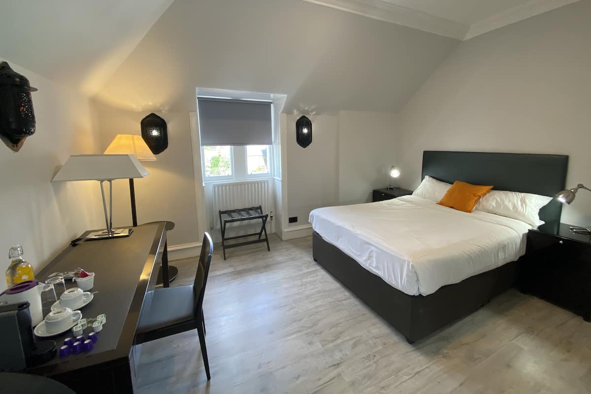 A bedroom with a bed, bedside tables, a desk with a chair, a lamp, and a radiator.