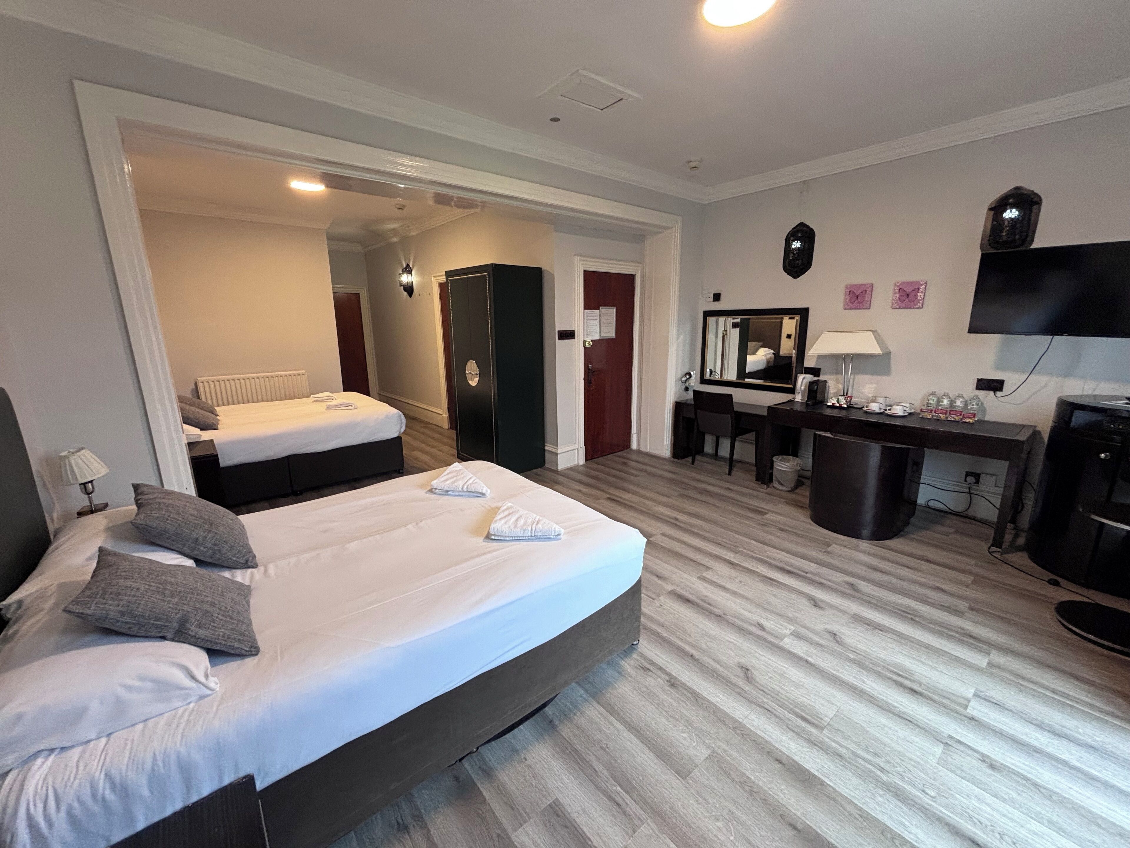 A hotel room with a large bed, a desk, a chair, a TV, and a mirror.