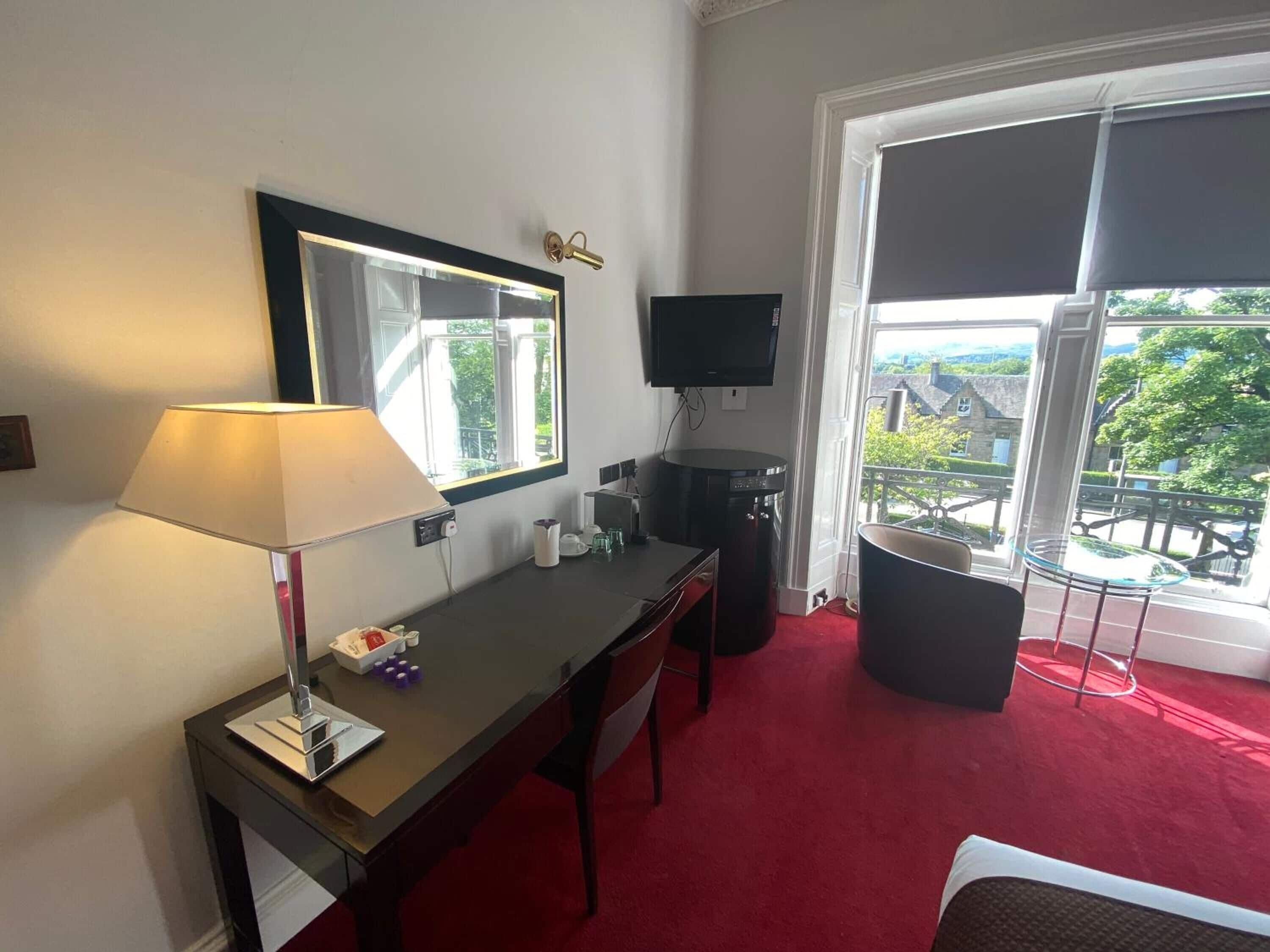 Una habitación de hotel con escritorio, televisión, un amplio ventanal con vistas y alfombra roja.