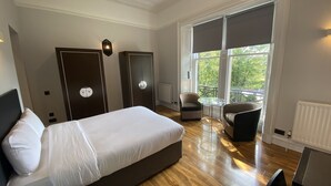 Een slaapkamer met een bed, twee kledingkasten, een stoel, een kleine tafel en een balkon met uitzicht.