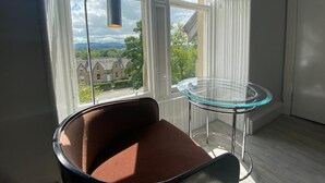 Een moderne kamer met een bruine stoel, een glazen tafel en uitzicht op gebouwen door een raam.