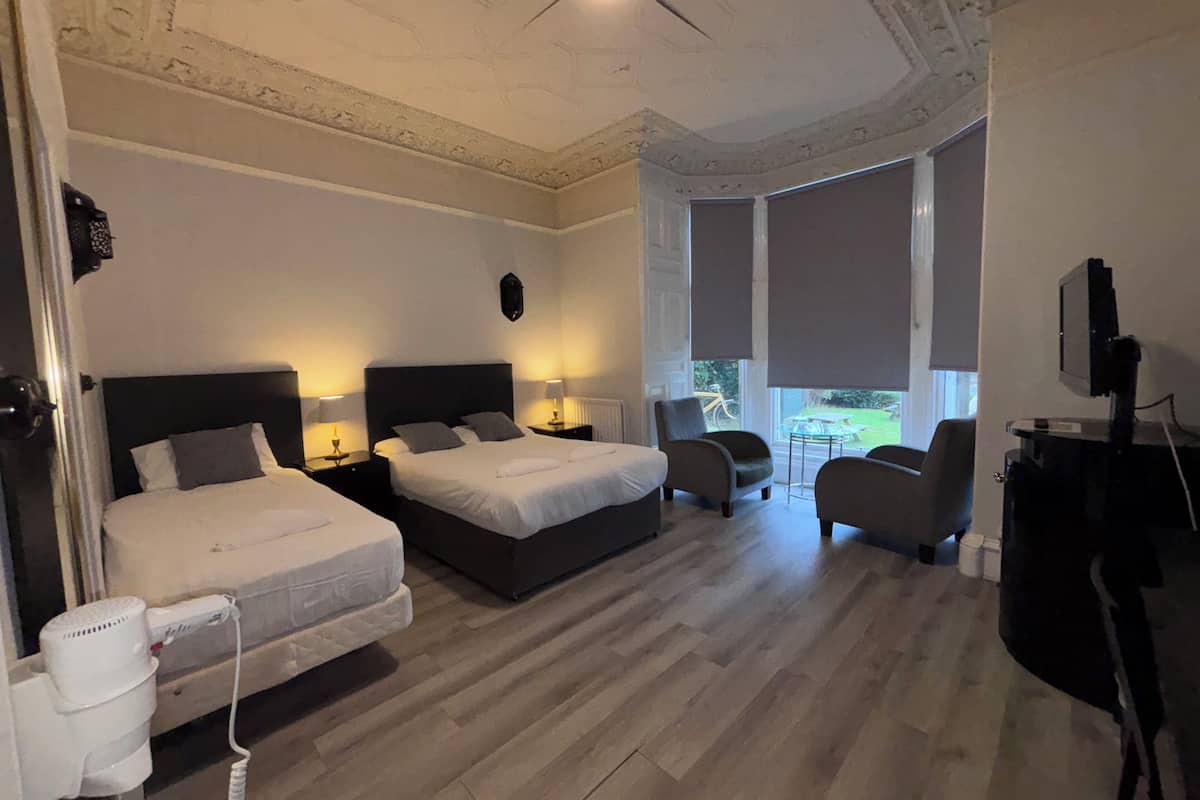 A hotel room with two beds, a seating area with chairs, a TV, and a view of the outdoors.