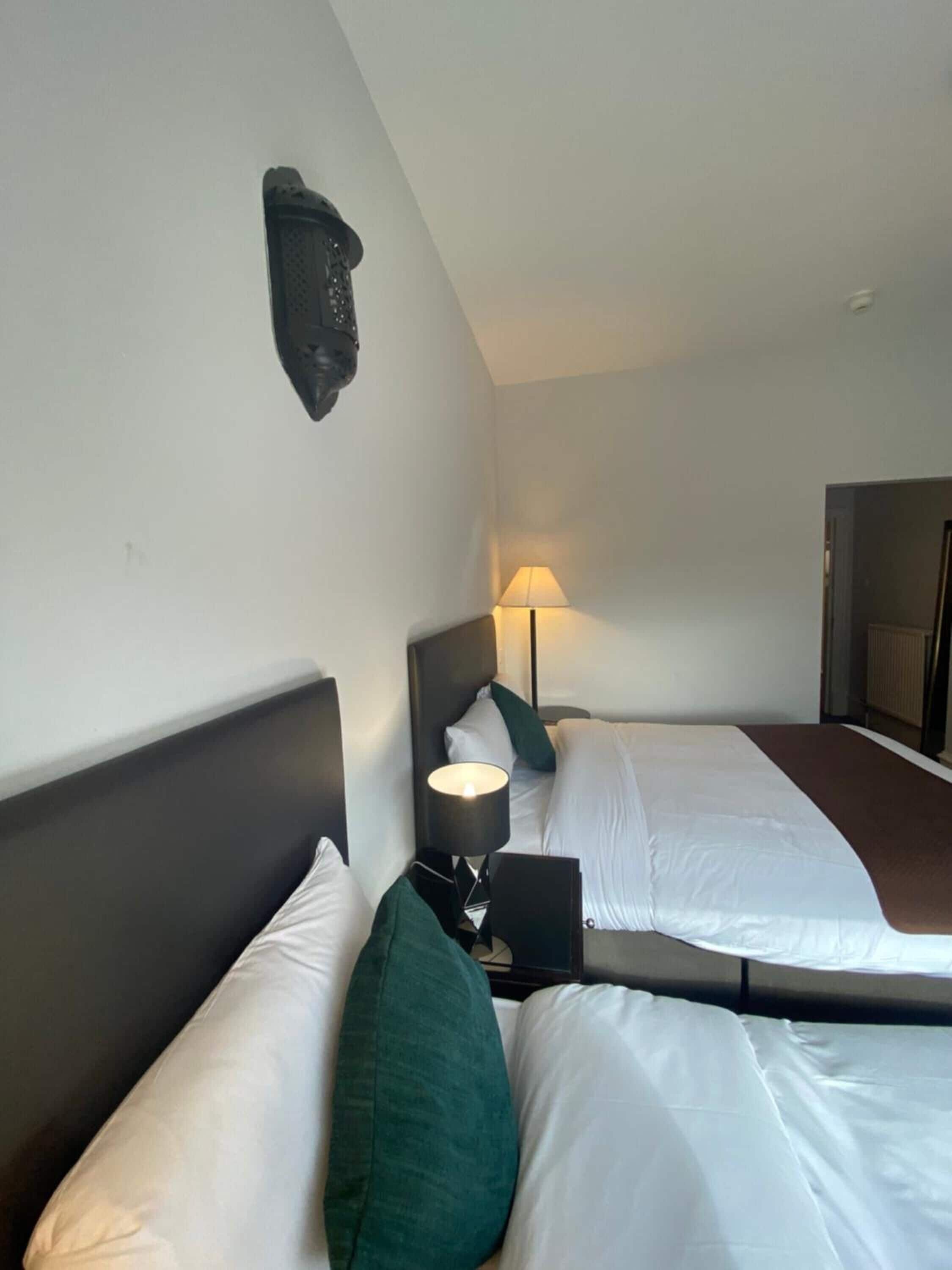 A hotel room with two beds, a wall-mounted light fixture, and a door to the right.