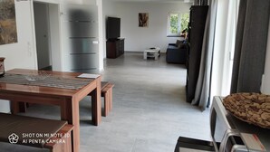A spacious living area with a wooden dining table, a sofa, and a television. - Ferienwohnung bis 4 Personen, Balkon, 75 qm (Fridolfing)