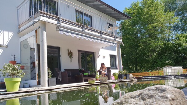 A two-story house with a balcony, a pool, and potted plants. - Ferienwohnung bis 4 Personen, Balkon, 75 qm (Fridolfing)