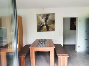 A modern dining area with a wooden table, benches, and a painting on the wall.
