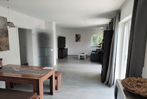 A spacious living area with a wooden dining table, a sofa, and a television.