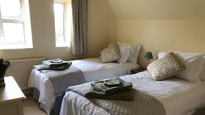 Une chambre double avec deux lits, chacun équipé d’une couette et d’oreillers, d’une table de chevet, d’une lampe et d’une fenêtre avec des rideaux.