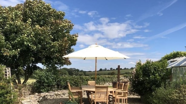 Une terrasse avec une table et des chaises, un puits en pierre et un grand arbre.