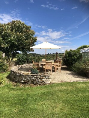 A patio with a table and chairs, a stone well, and a large tree. - Beautiful 3 Bedroomed Cotswolds Farmhouse (Cheltenham)