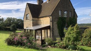 Une maison à deux étages, dotée d’un toit en pente, d’un porche abrité et d’un jardin agrémenté de plantes à fleurs.