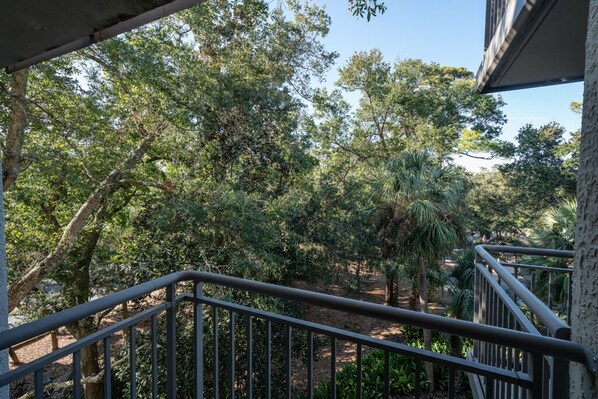A balcony with a metal railing overlooking a garden with various trees and shrubs.
