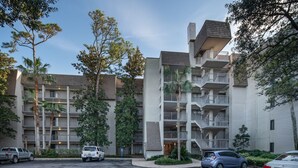 Edificio residencial de varios pisos con balcones, espacios de estacionamiento y zonas verdes circundantes.
