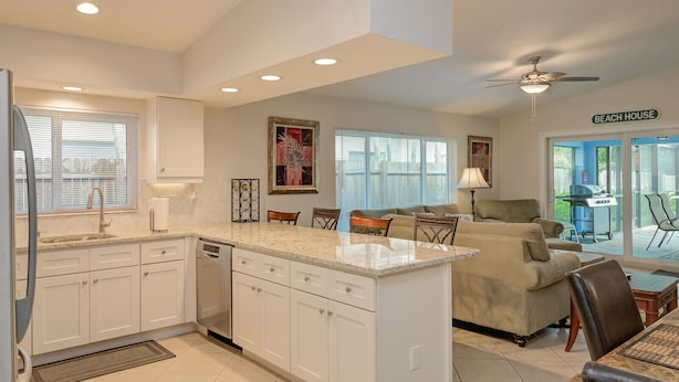 A modern kitchen with white cabinets, a granite countertop, and a dining area with a sofa and chairs. - 3 Bedroom, Huge Pool, Hot Tub, Screened in Lanai in the coveted 500 block (Naples)