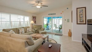 A living room with a sofa set, a coffee table, and a TV stand. There is a ceiling fan, a lamp, and a sign that reads "BEACH HOUSE". - 3 Bedroom, Huge Pool, Hot Tub, Screened in Lanai in the coveted 500 block (Naples)