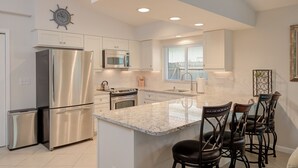 A modern kitchen with stainless steel appliances, a central island with bar stools, and a decorative clock on the wall. - 3 Bedroom, Huge Pool, Hot Tub, Screened in Lanai in the coveted 500 block (Naples)