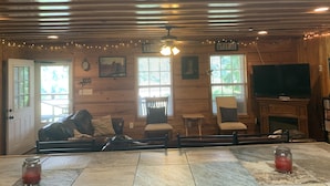 A cozy cabin interior with a wooden ceiling, a fireplace, a television, and a dining area with a table and chairs. - The Leaf River Yacht Club (Petal)