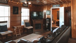 A cozy cabin-style room with a wooden ceiling, a television, a fireplace, a couch, and a bookshelf. - The Leaf River Yacht Club (Petal)