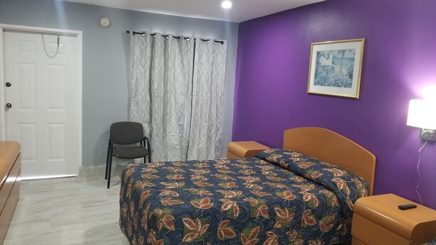 Een slaapkamer met een bed, een stoel, een nachtkastje en een aan de muur hangend schilderij.