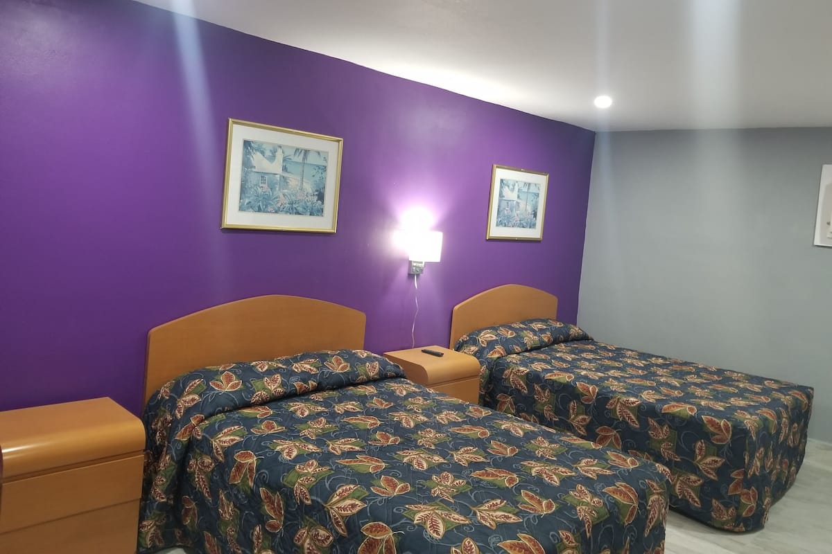 Habitación con dos camas, paredes moradas y dos cuadros en la pared.
