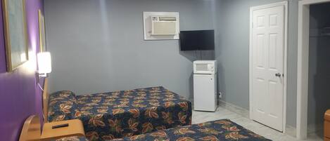 Een kamer met twee bedden, een kleine witte koelkast, een magnetron, een televisie en een deur.