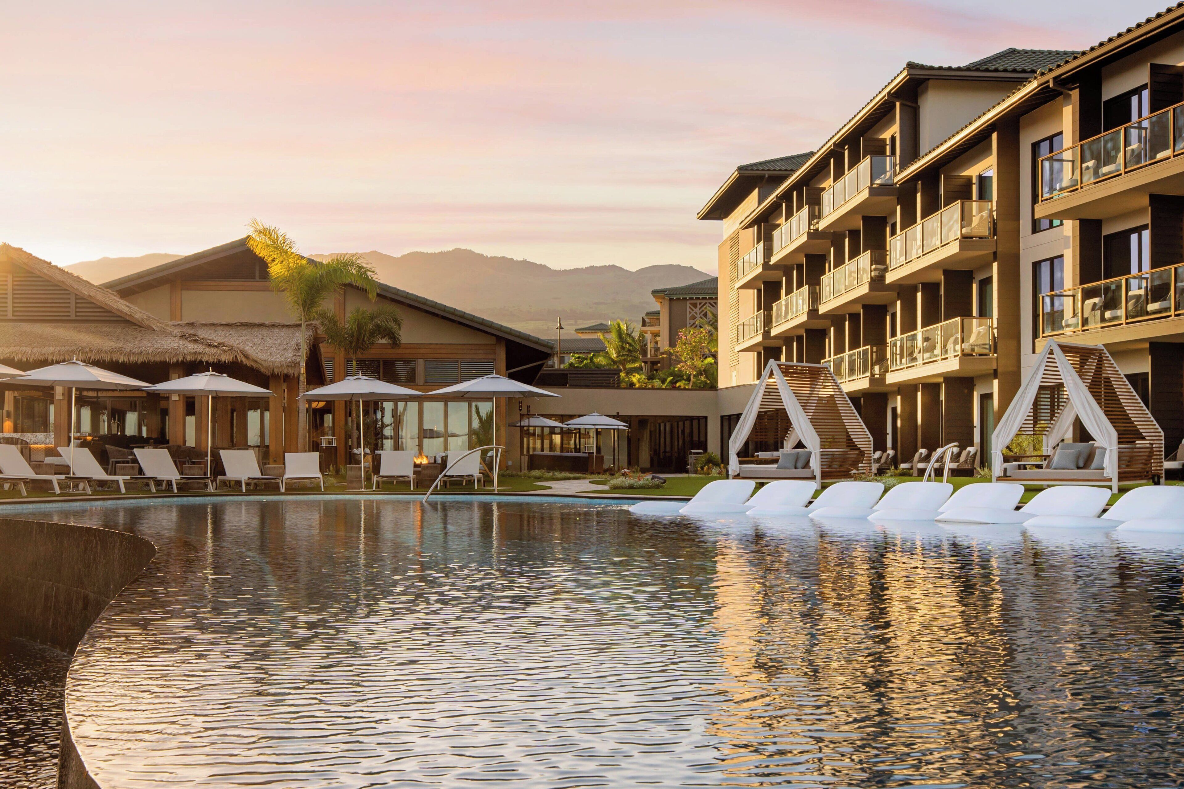 A resort with a swimming pool, lounge chairs, and a mountain backdrop.