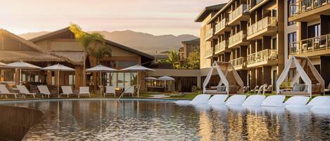 Un resort con piscina, tumbonas y montañas al fondo.
