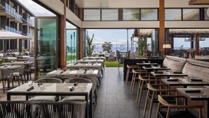 Un restaurante con terraza y vistas panorámicas, con mobiliario moderno y un área de comedor con paredes de vidrio.