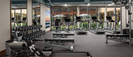 A modern gym with various exercise equipment, large windows, and a view of the outdoors.