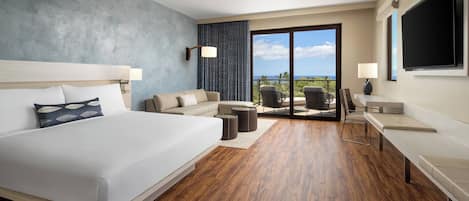 A hotel room with a large bed, a sofa, a desk, and a balcony with a view.