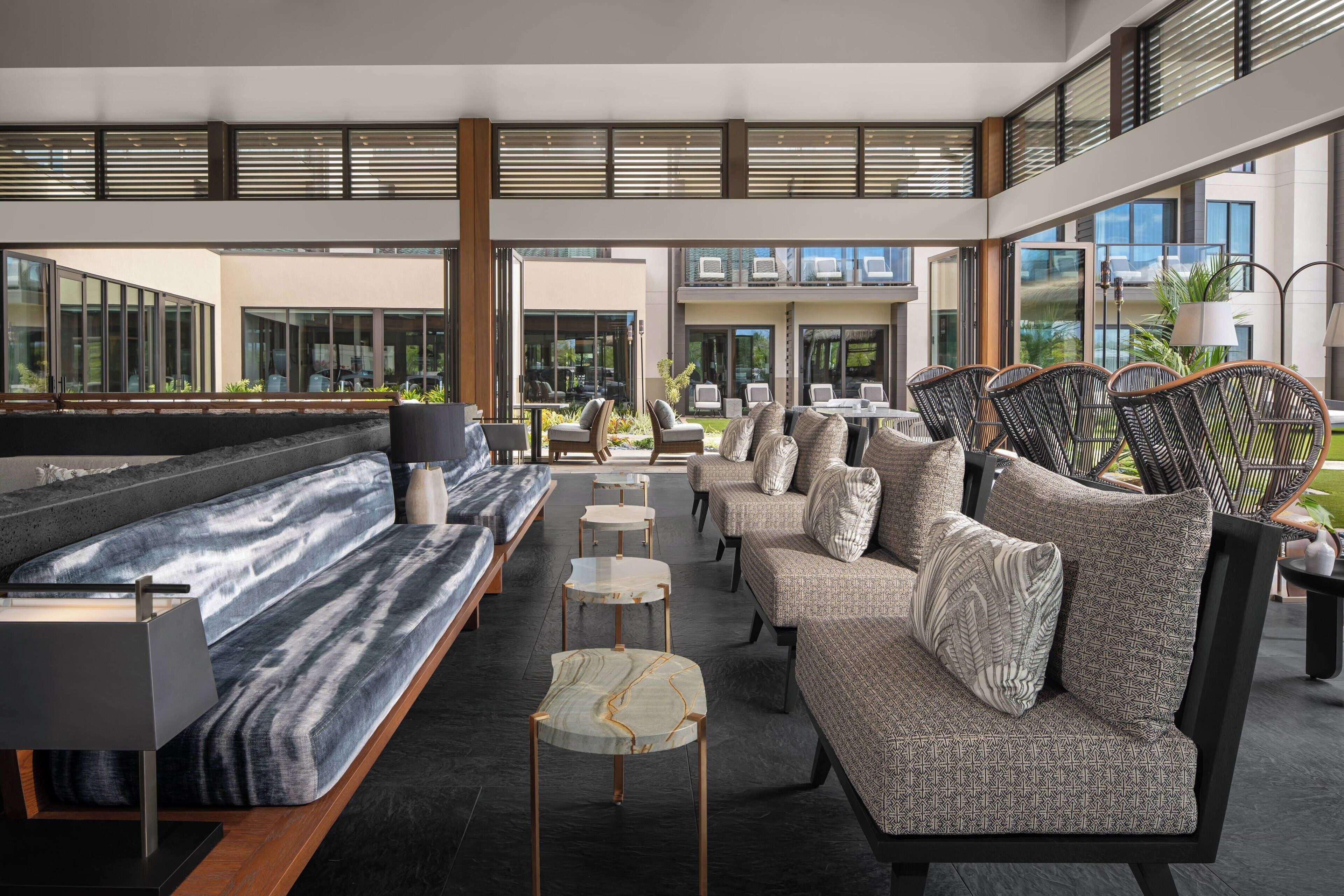 A modern indoor seating area with sofas and tables, large windows, and a view of the outside.