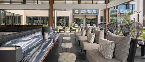 A modern indoor seating area with sofas and tables, large windows, and a view of the outside.