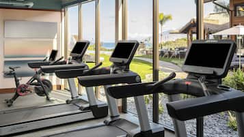 Una palestra con tapis roulant e ellittica, ampie finestre con vista sull'oceano e su una zona resort.