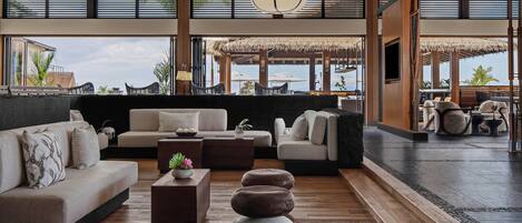 Un vaste espace de détente au design moderne, comprenant un grand canapé, une table basse et un coin salon agrémenté de parasols en chaume.