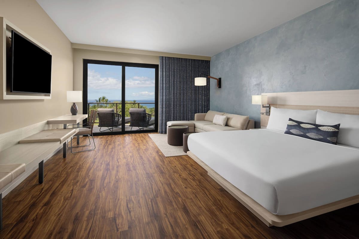 Una habitación de hotel moderna con una cama grande, un escritorio, una silla y un balcón con vistas.