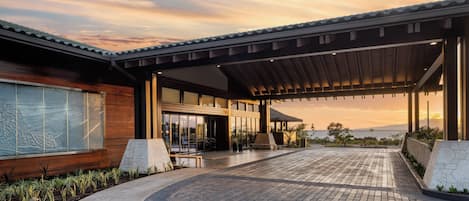 A modern building with a covered entrance, a paved walkway, and a view of the landscape.
