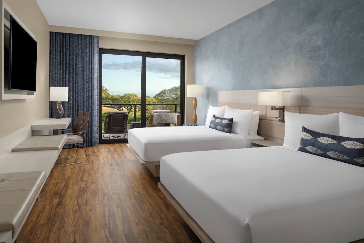 Habitación de hotel con dos camas, zona de estar, televisión y balcón con vistas.