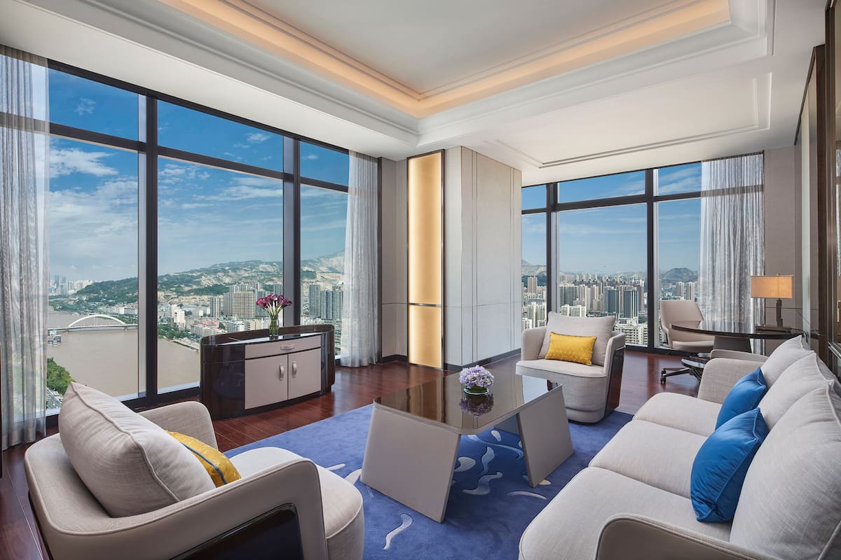 A spacious living room with large windows offering a city view, a modern coffee table, and comfortable seating.