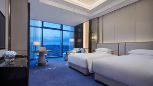 A hotel room with two beds, a desk with a lamp, a chair, and a view of the cityscape through large windows. - Hyatt Regency Lanzhou (Lanzhou)