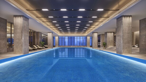 A modern indoor swimming pool with a long, rectangular shape, surrounded by lounge chairs and a city view. - Hyatt Regency Lanzhou (Lanzhou)