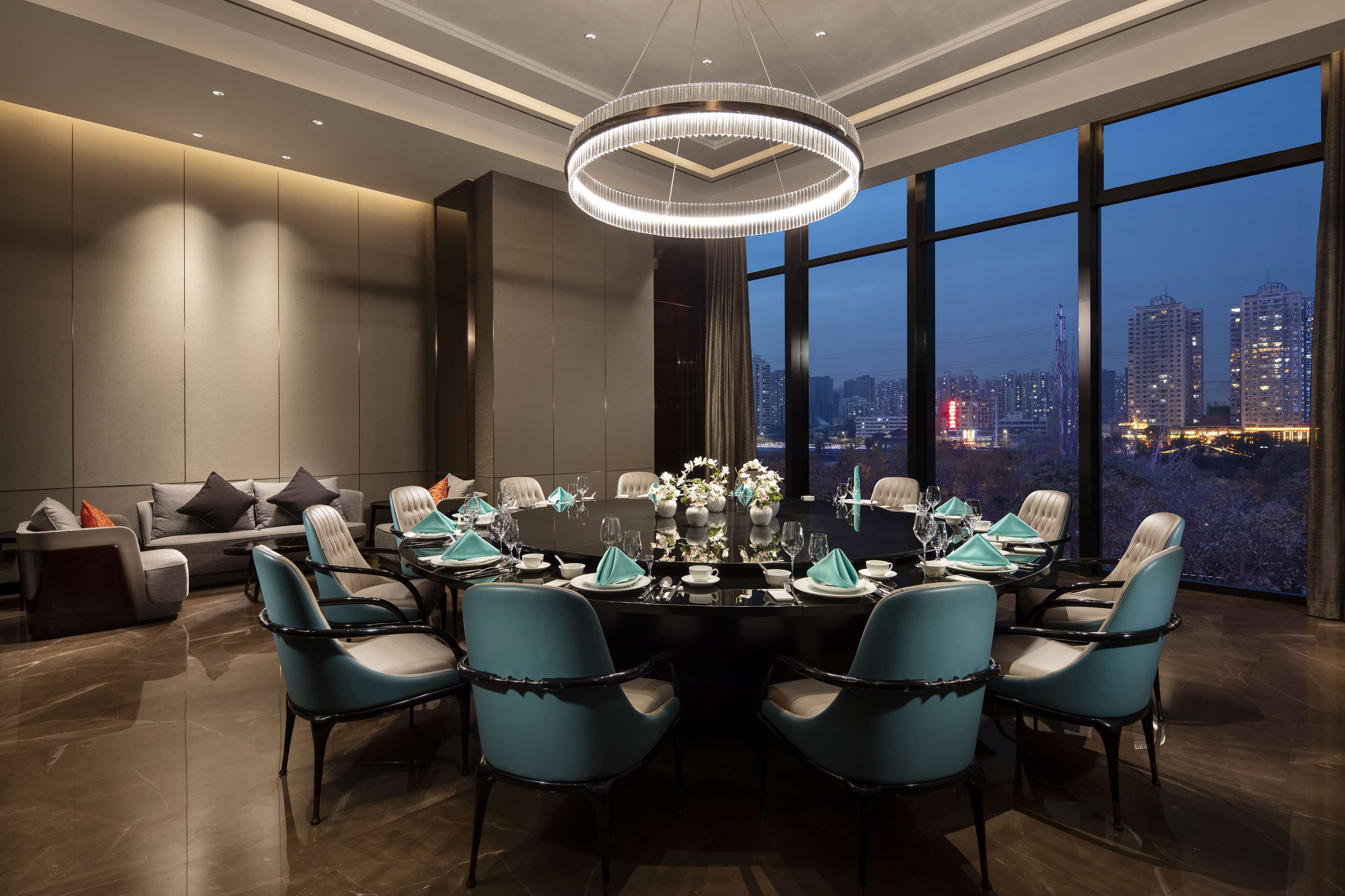 A modern conference room with a round table, blue chairs, and a city view through large windows.