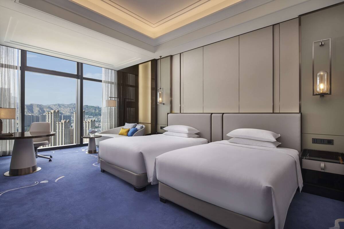 A hotel room with two beds, a desk, and a view of the city.