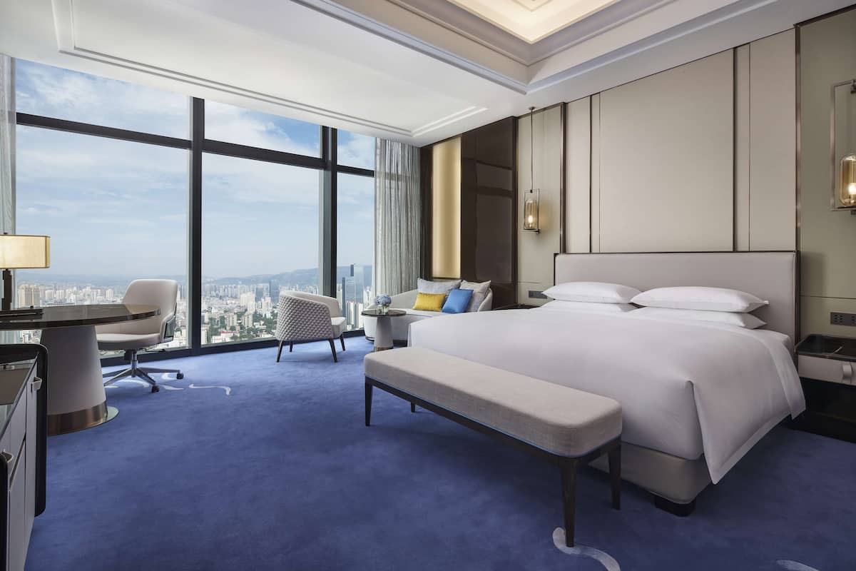 A hotel room with a large bed, a desk, a chair, and a view of the city.