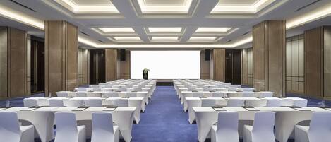 A conference room with rows of white chairs, a blue carpet, and a modern ceiling design.