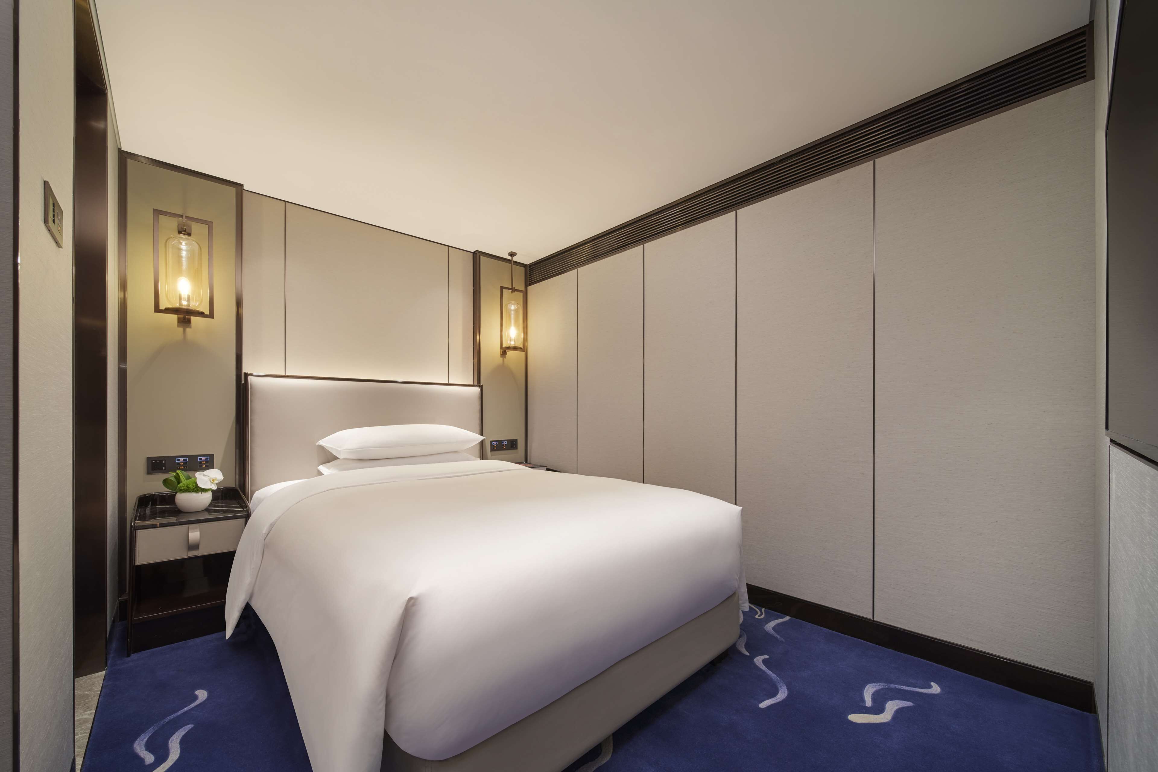A hotel room with a large bed, a nightstand with a lamp, and a wall-mounted mirror.