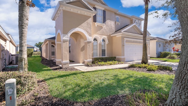 A two-story house with a beige exterior, a garage, and a well-maintained lawn.