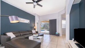 A modern living room with a sectional sofa, a coffee table, a flat-screen TV, and a ceiling fan.