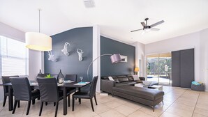A modern living room with a dining area, a sofa, and a ceiling fan.