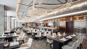 Un vaste espace de restauration dans l’hôtel, avec de nombreuses tables et chaises, un bar central et un grand lustre décoratif.